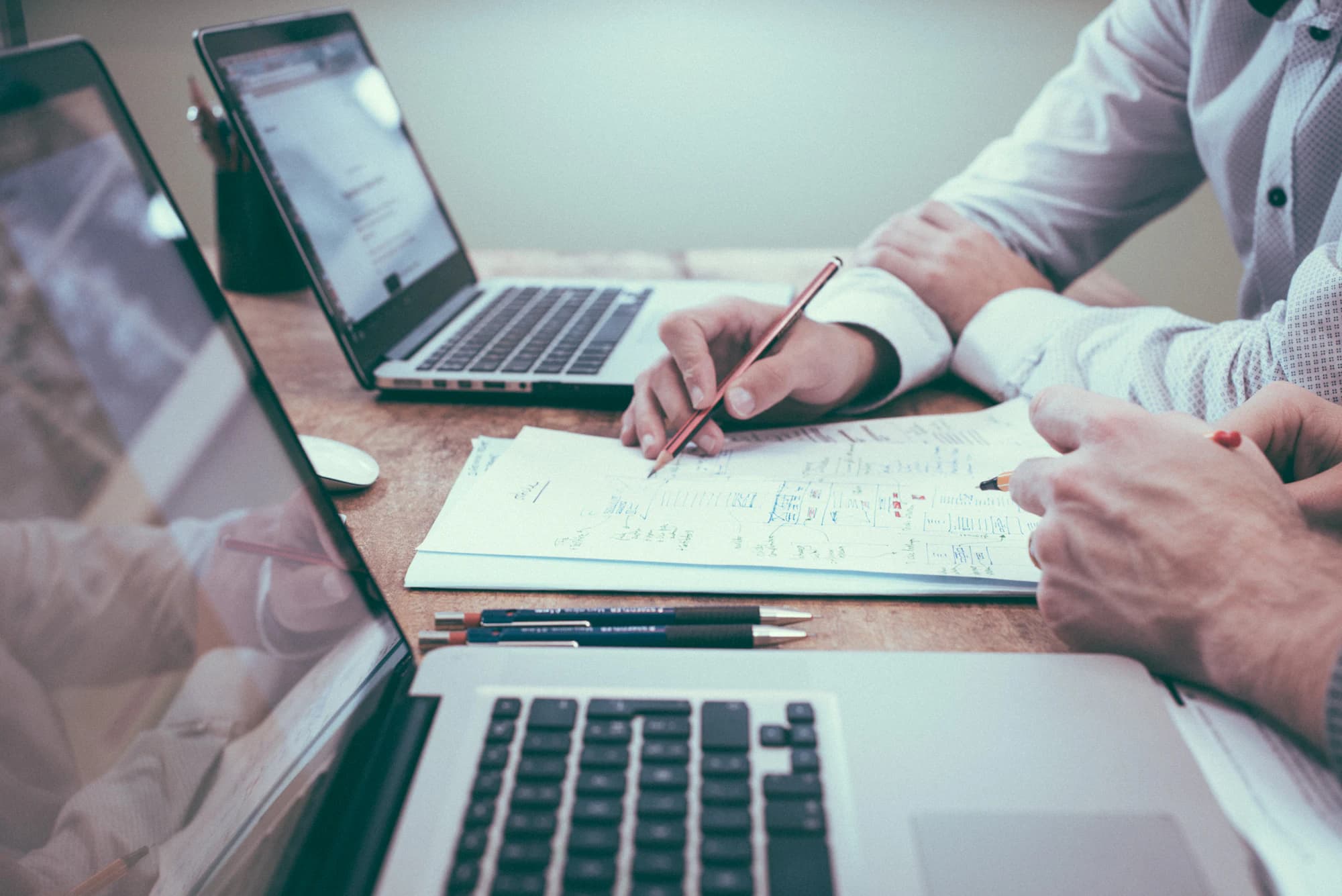 Two people working through printed statements and laptops across a desk.