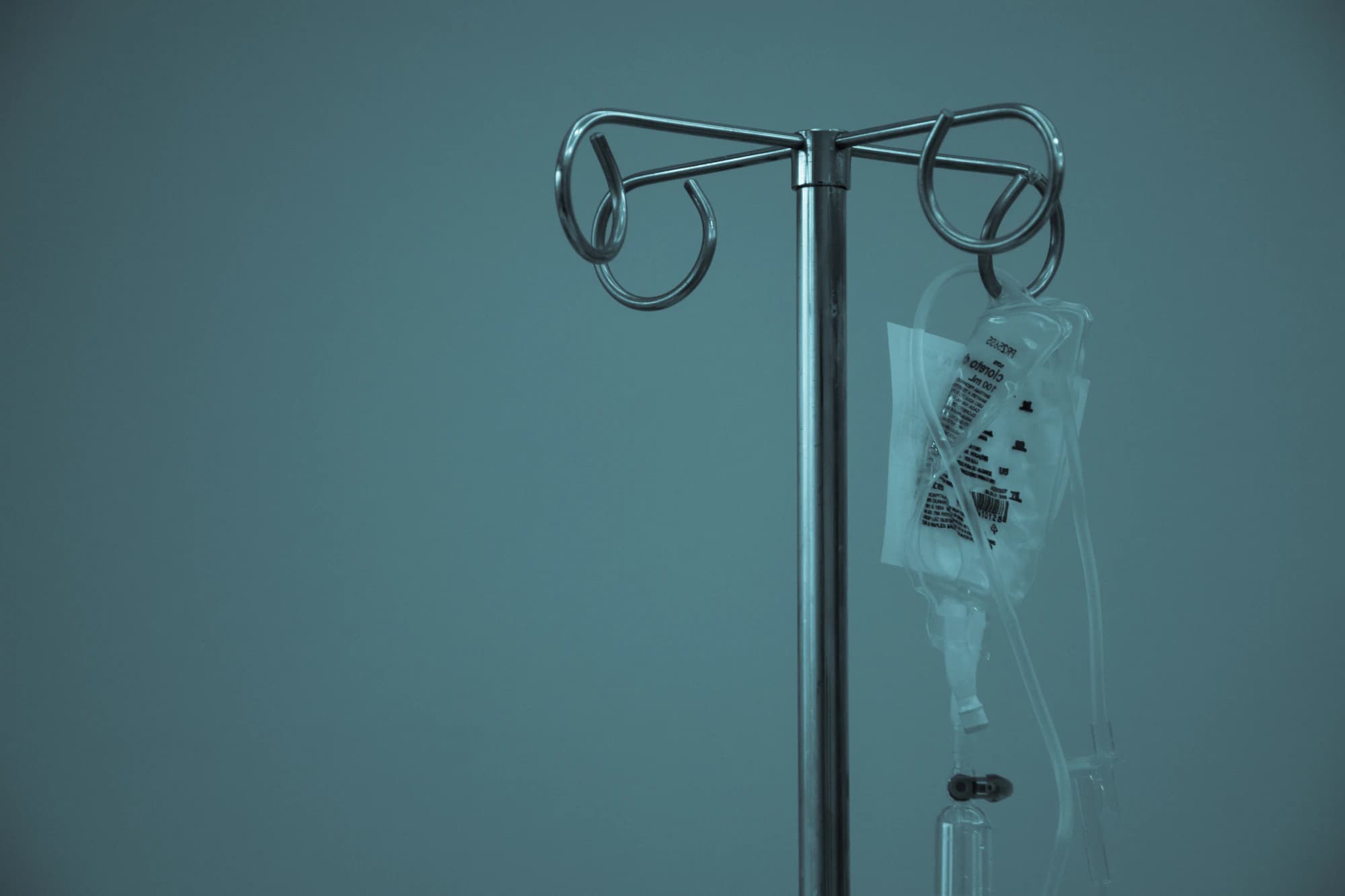 An intravenous stand with a fluid bag hanging in a dim room.