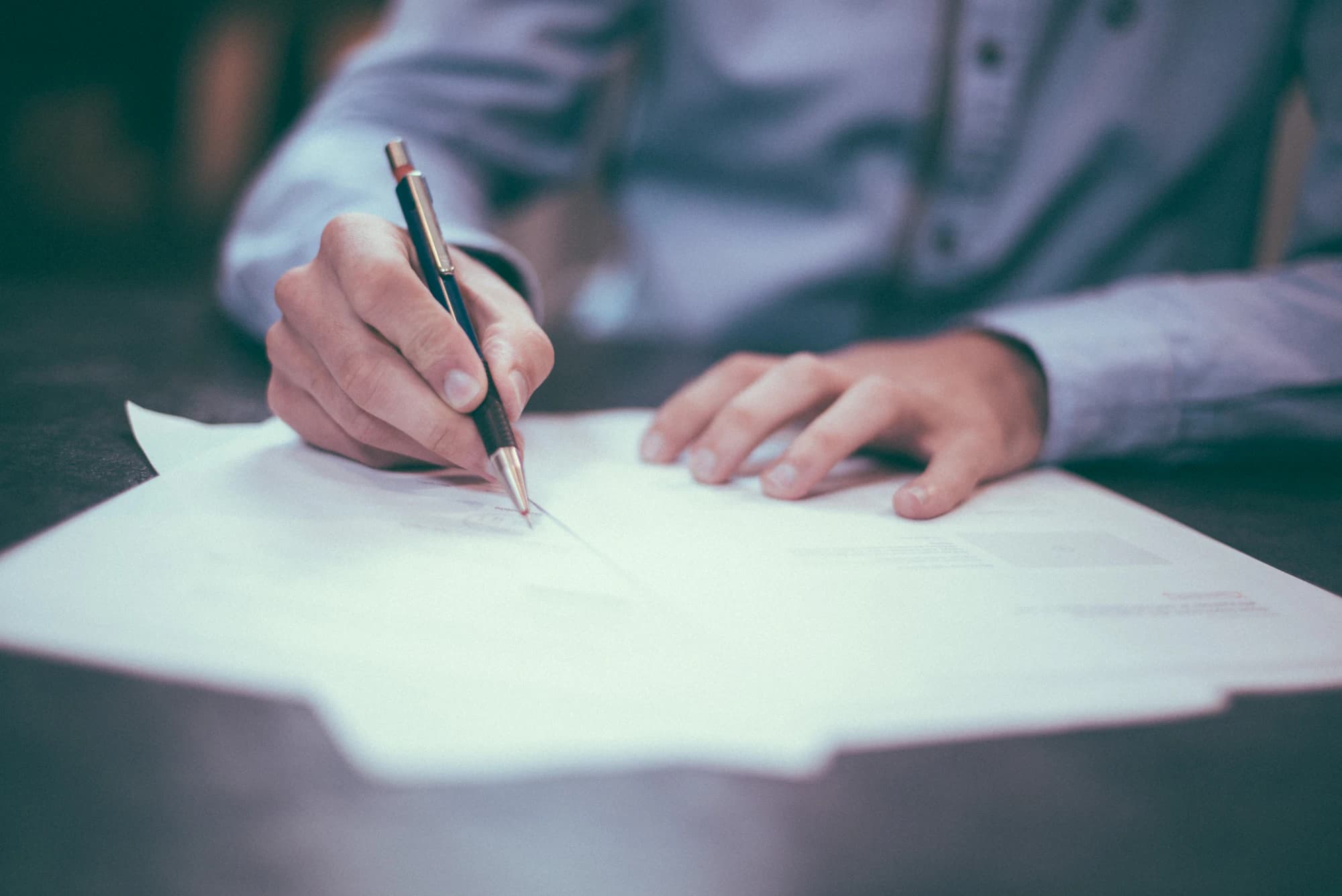 A hand signing a printed document on a plain desk.