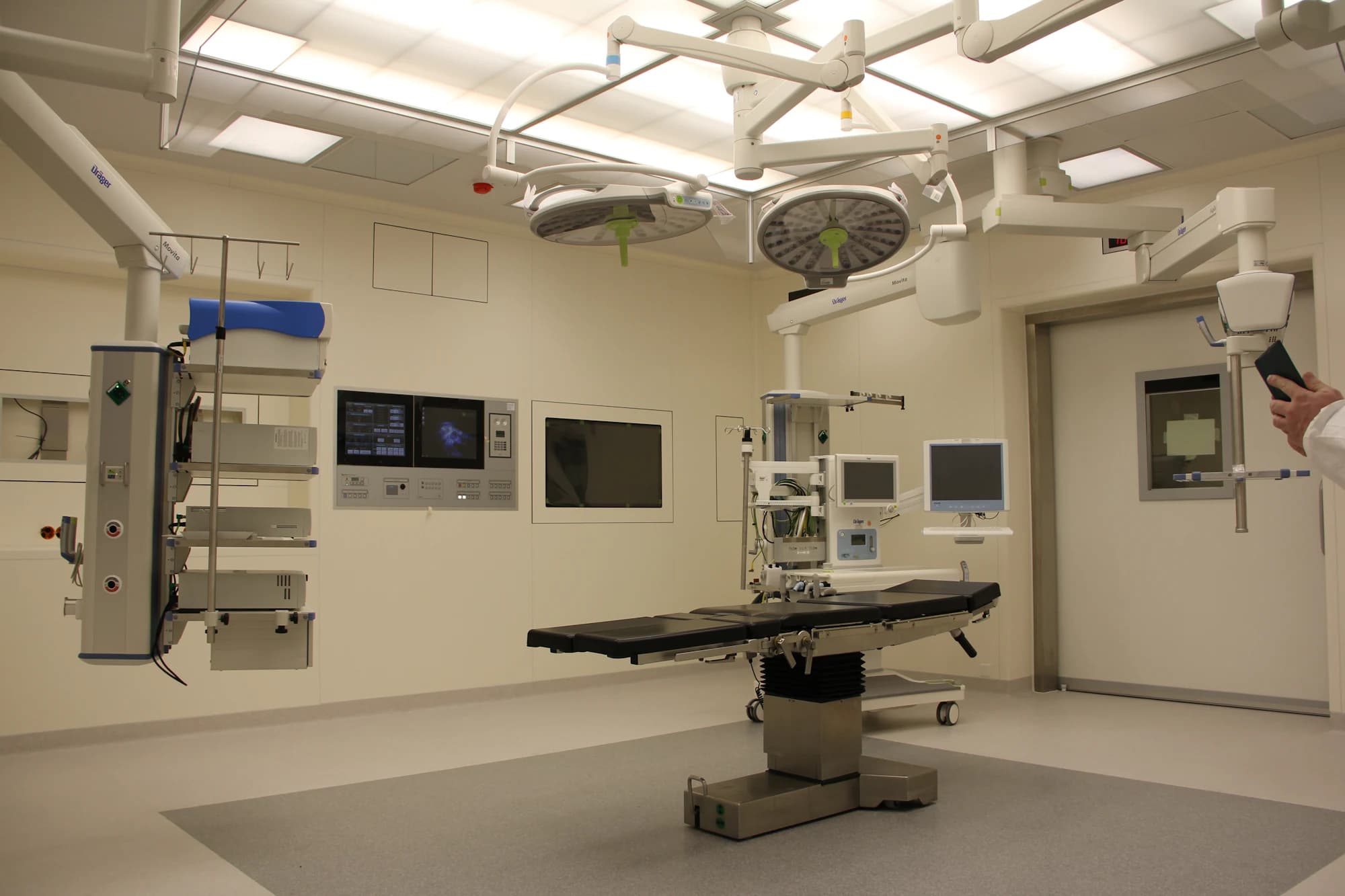 An empty operating theatre with the table under the surgical lights and equipment booms overhead.