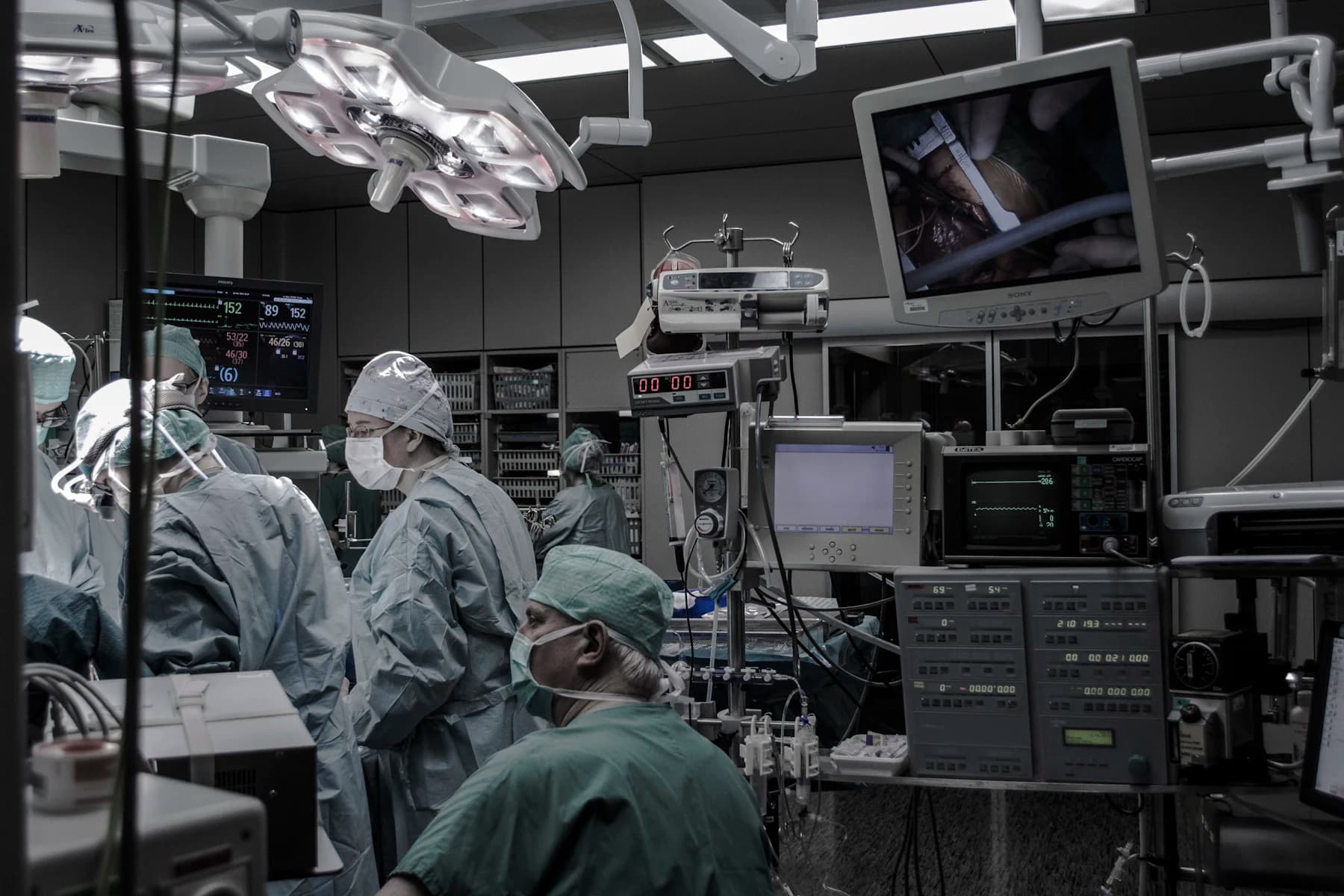 A darkened critical care suite with monitors, screens and staff at the bedside.