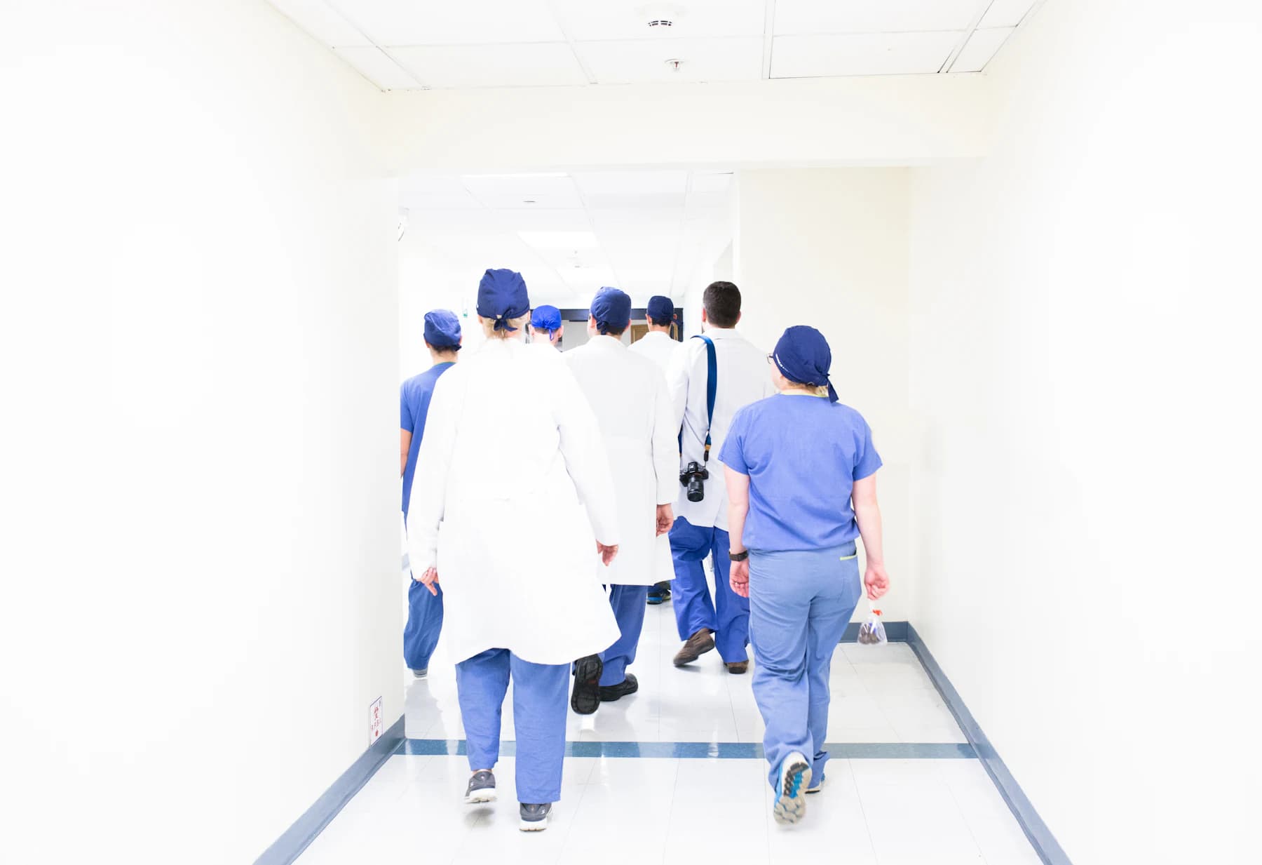 Hospital staff moving down a corridor towards a set of doors.