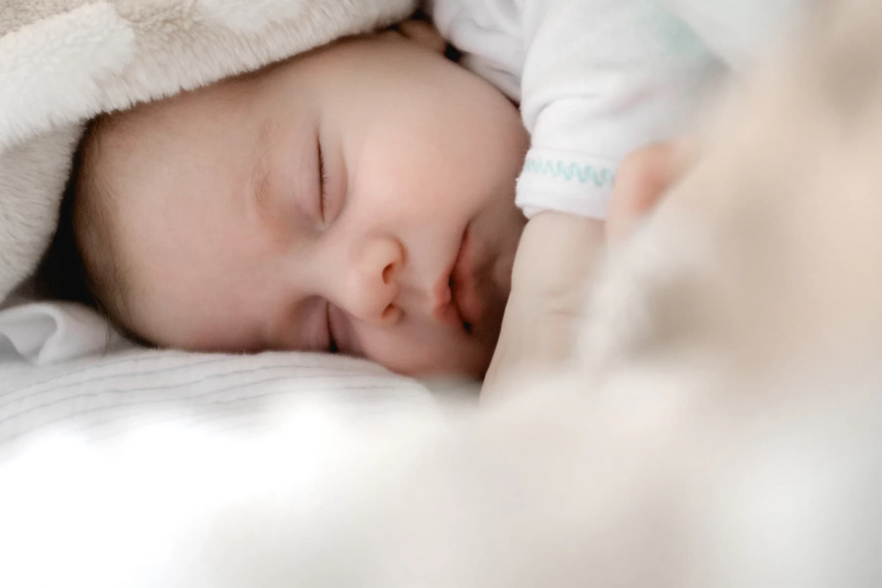A newborn asleep under a cot blanket in a neonatal unit.