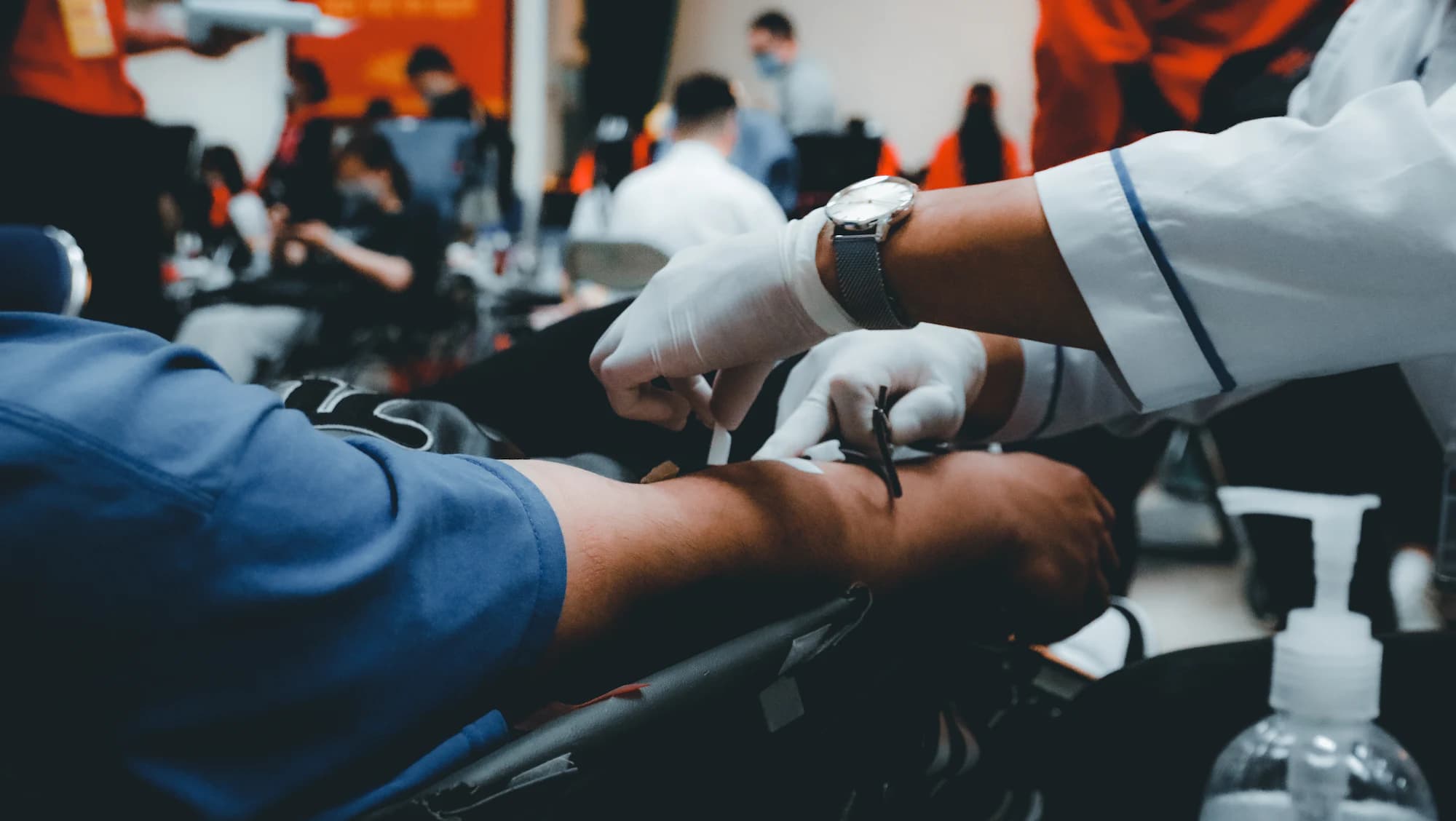 A phlebotomist in gloves preparing a donor's arm for collection at a blood donation drive.