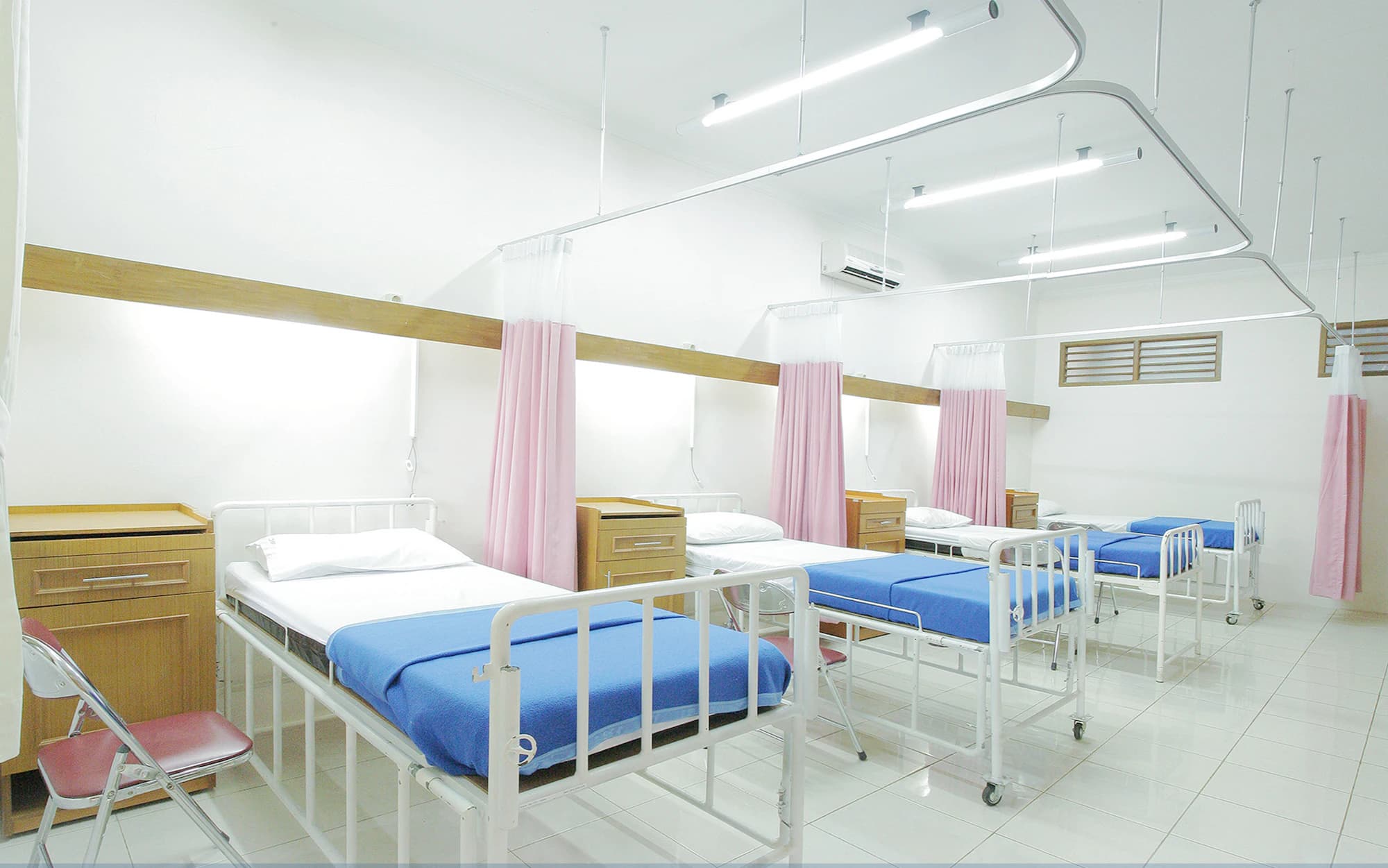 An empty hospital ward with four made beds and drawn curtains.