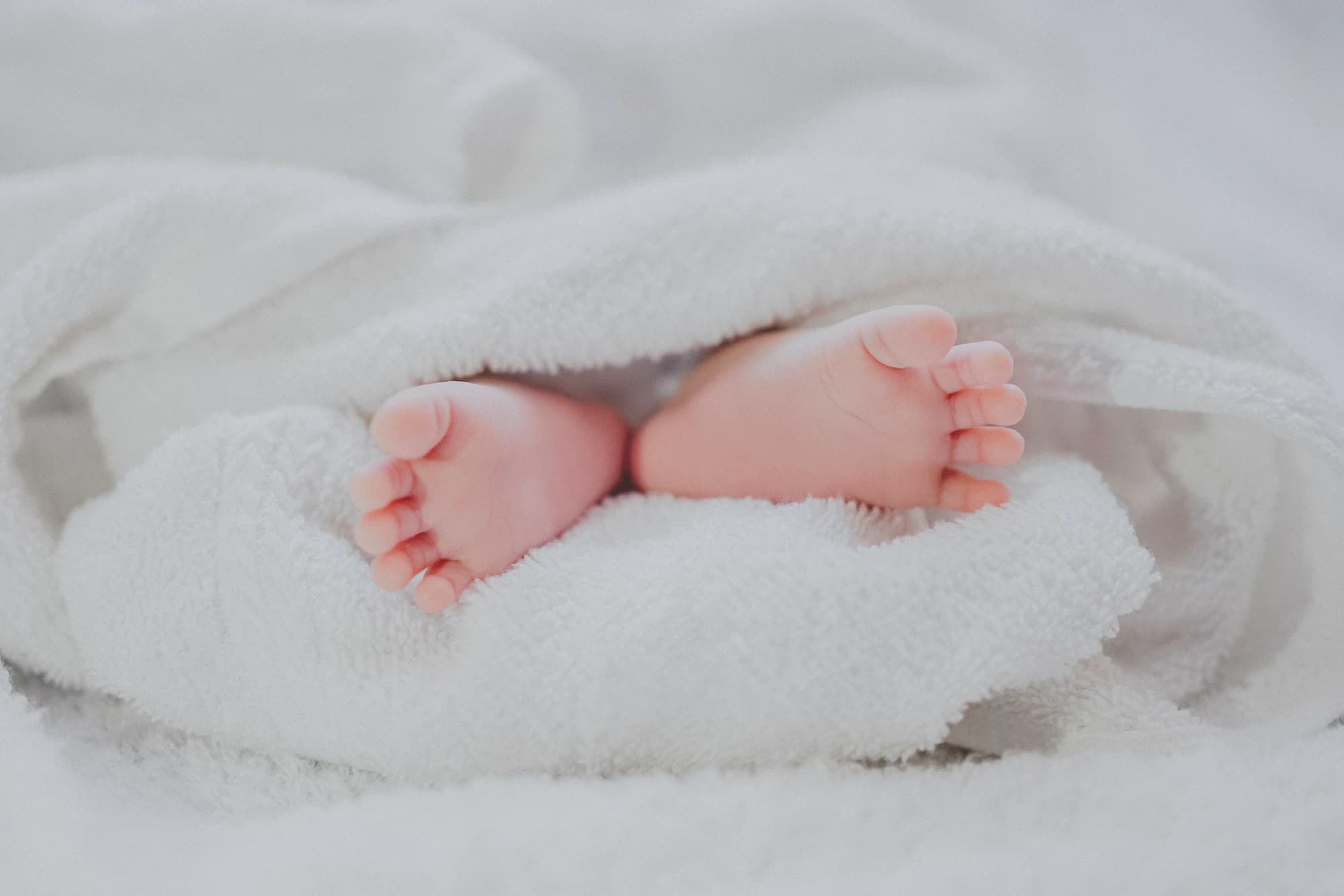 A newborn's feet wrapped in a white blanket, photographed close and softly lit.