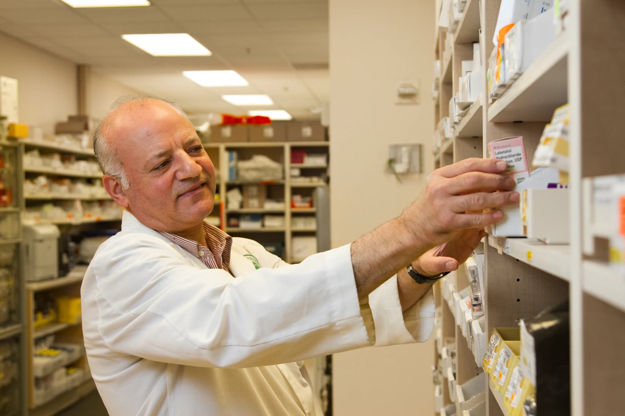 A pharmacist reaching for a box on a dispensing shelf in a hospital pharmacy store.