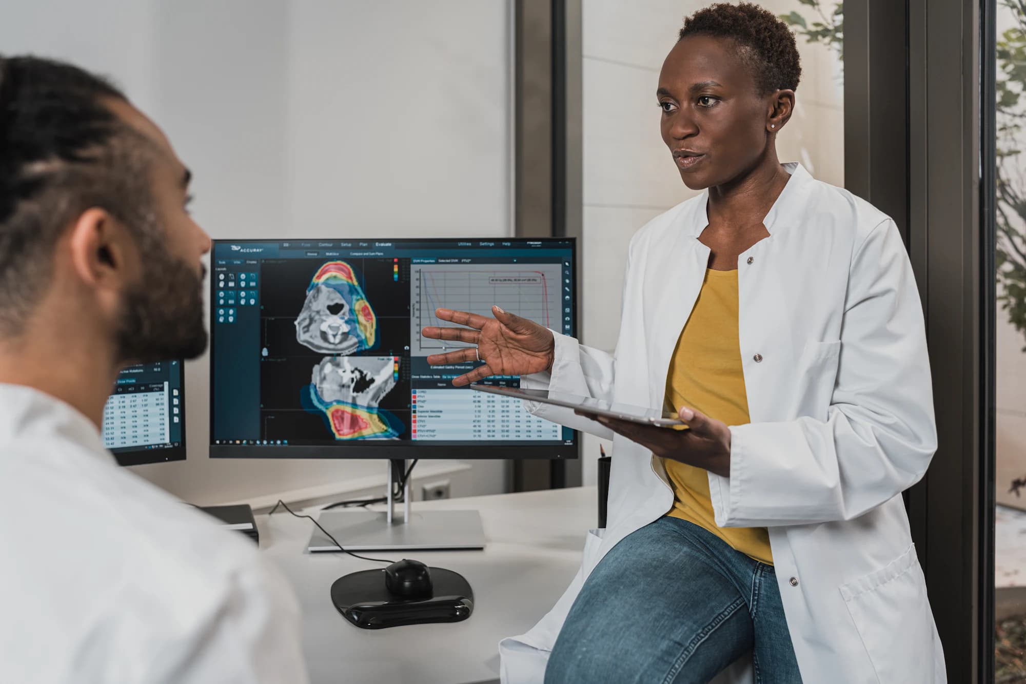 Two radiologists at a reporting workstation discussing a cross-sectional study on the screens in front of them.