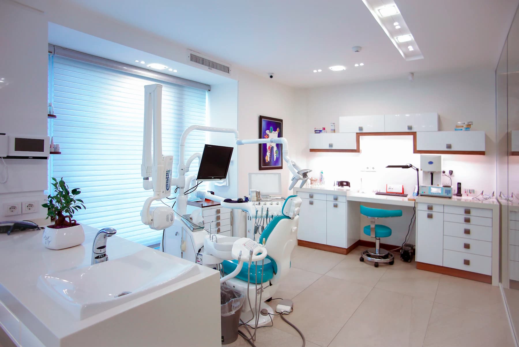 A clinical treatment room with an examination chair, instrument tray and screen.