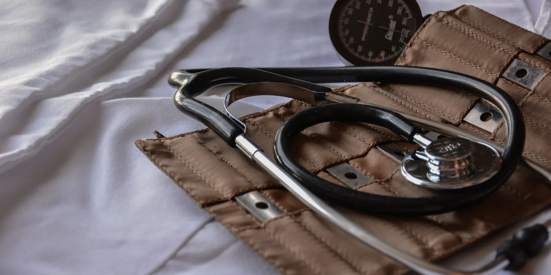A stethoscope and a blood pressure cuff left on a made bed.