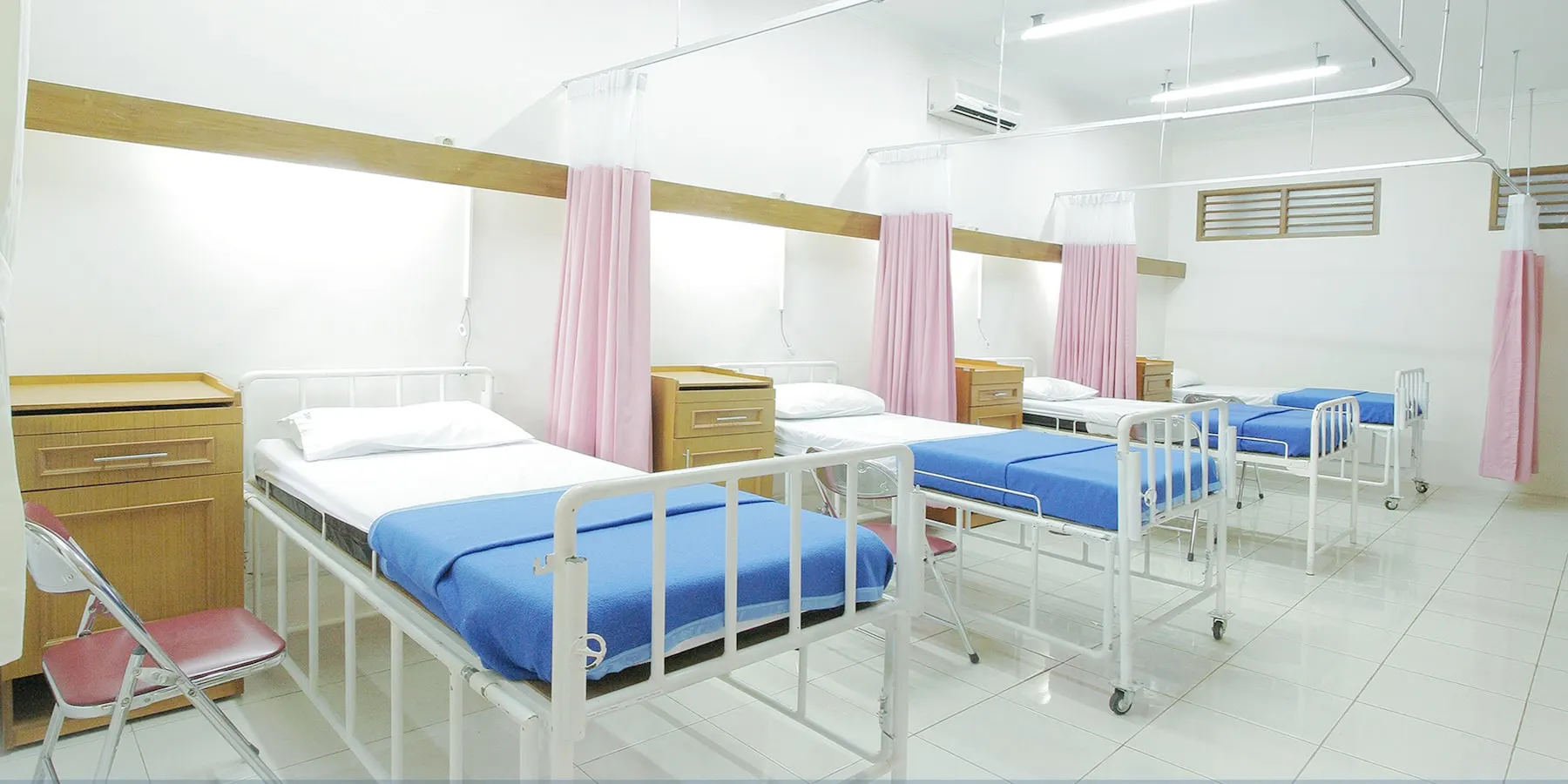 An empty general ward, beds made and curtains drawn back.